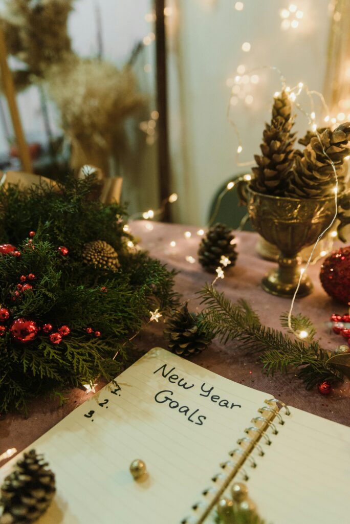Notebook with New Year goals surrounded by festive Christmas decorations and lights.