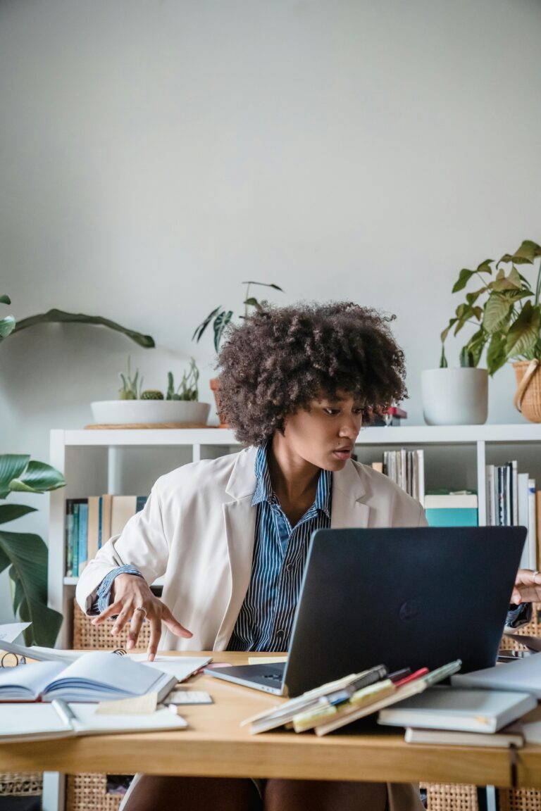 Businesswoman working efficiently at her desk with plants and books around, showcasing focus and productivity.